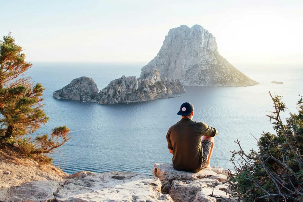 Mann sitzt auf einer Klippe und schaut aufs Meer