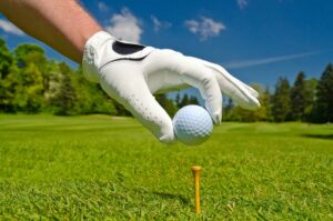 Hand platziert Golfball auf Tee über schönen Golfplatz mit blauem Himmel