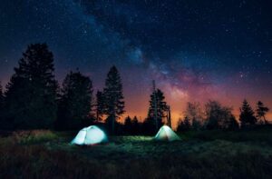 Zwei Zelten stehen in der Nacht im Wald mit einem Sternenhimmel darüber