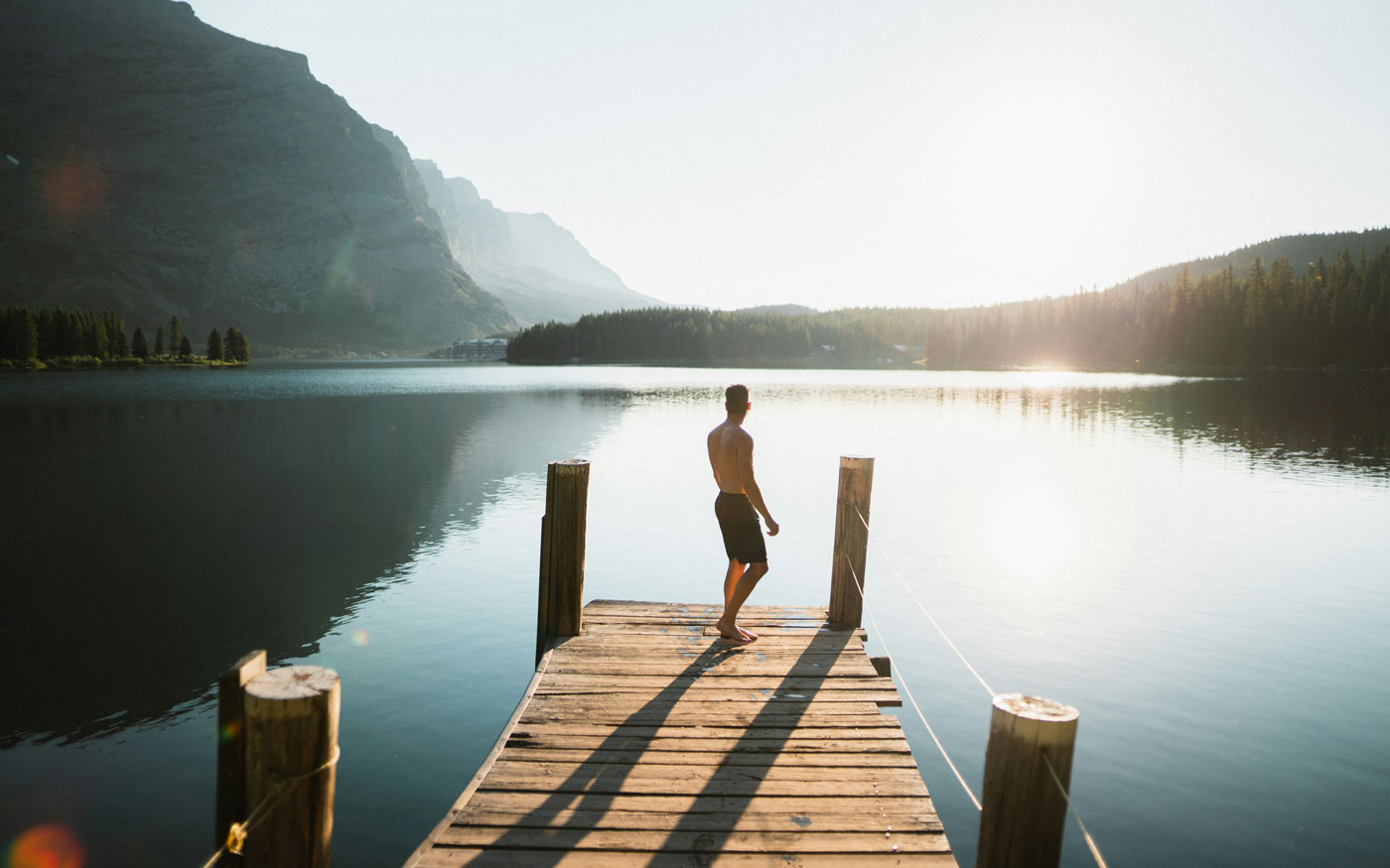 Junger Mann steh auf einem Steg am See in einer Badehose und möchte anbaden
