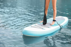 Junge Frau benutzt aufblasbares SUP Board zum Surfen auf dem See
