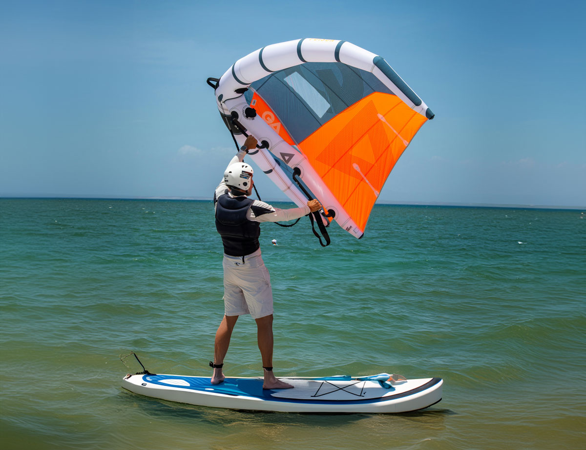 Mann steht auf seinem Stand Up Paddle mit dem Wing in der Hand