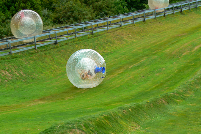 Zorbing Kugel rollt eine Wiese herab