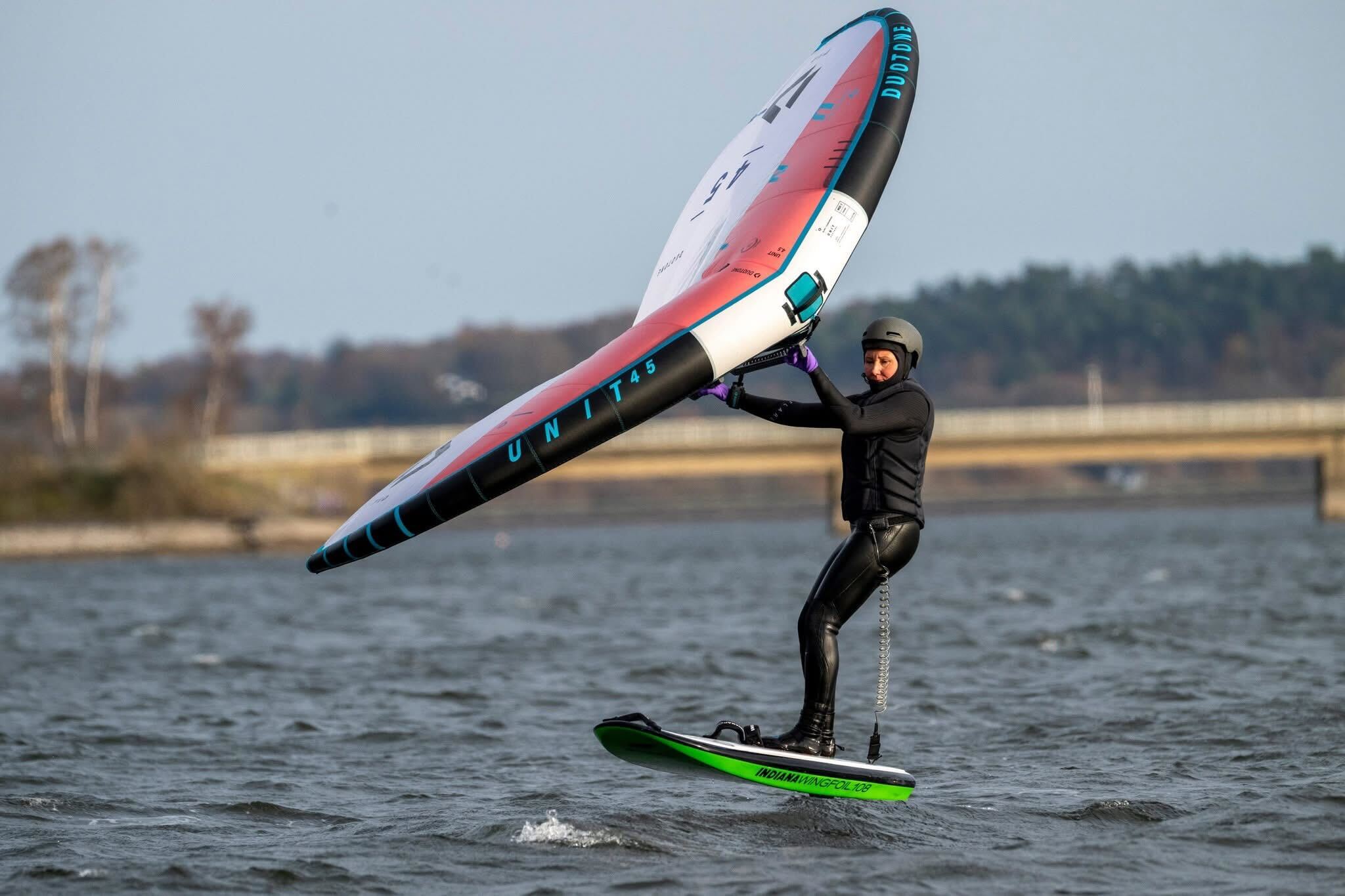 Frau surft auf einem Board mit einem Wing über einen See