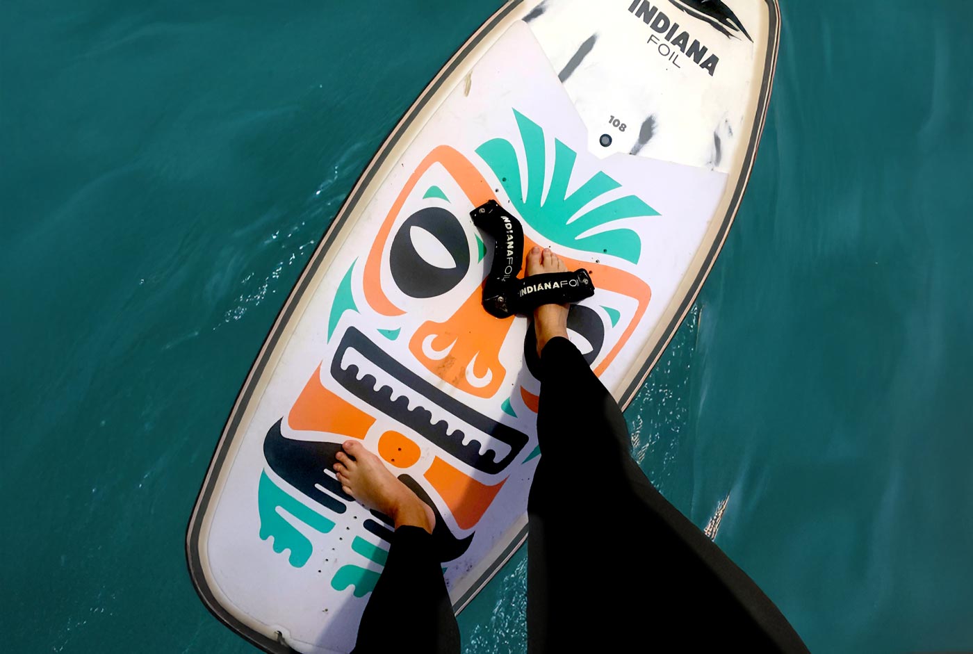 Frau steht auf einem Wingfoilboard, rechter Fuß vorne in der Schlaufe, linker Fuß hinten parallel zum Wingfoil Board